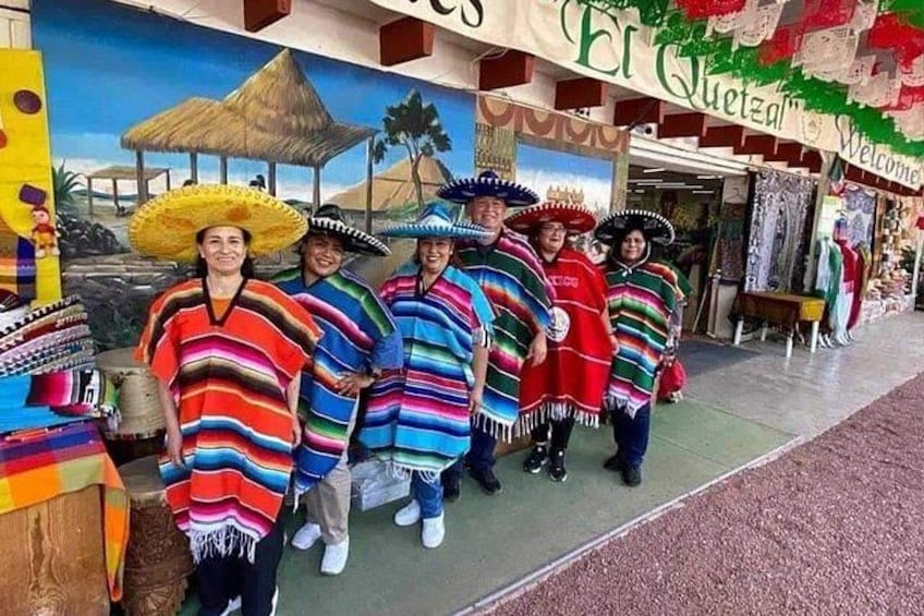 A group of people in traditional Mexican attire with a mural in the background. 4