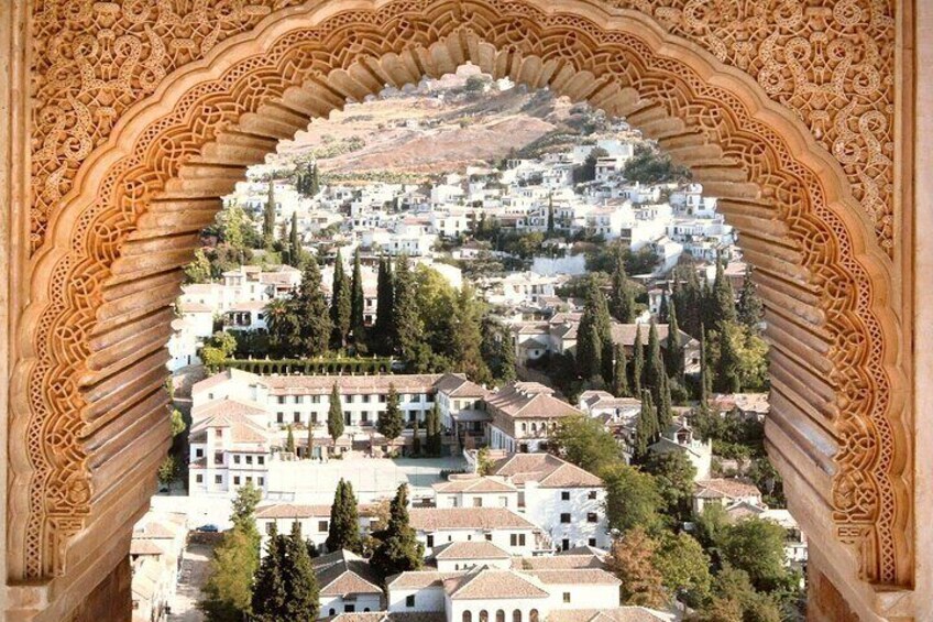 Una vista de un pueblo a través de un arco decorativo, con edificios blancos y árboles verdes. 2