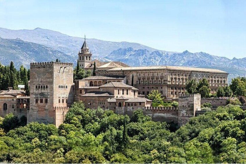 Un castillo histórico con torres y un edificio grande, rodeado de vegetación exuberante y montañas al fondo. 3