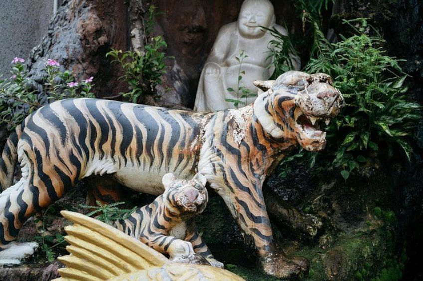 A tiger statue in a garden with greenery and a Buddha statue in the background. 3