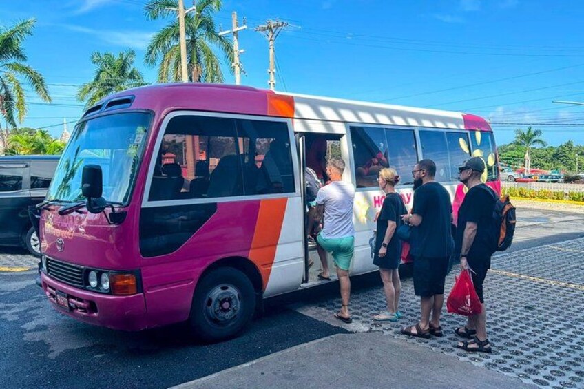 A pink and white bus with passengers boarding. 2