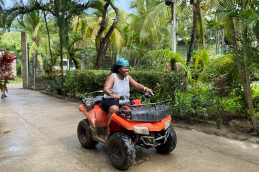 A person riding an orange ATV on a wet road surrounded by greenery. 5