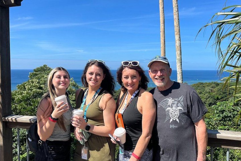 Four people standing on a wooden deck with a view of the ocean and palm trees. 2