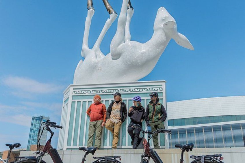 A large white sculpture of a horse, four people standing in front, and bicycles. 1