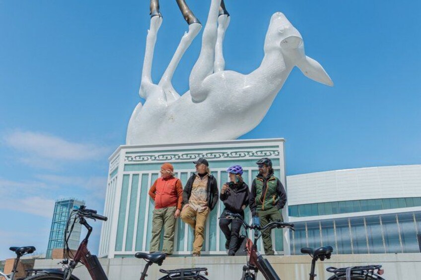 A large white sculpture of a whale, four people standing on a platform, and several bicycles. 1
