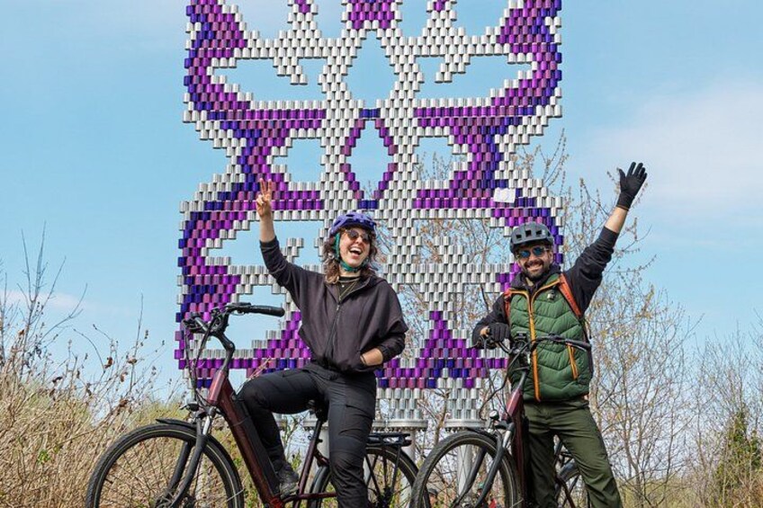 Two people on bicycles in front of a pixelated artwork. 3