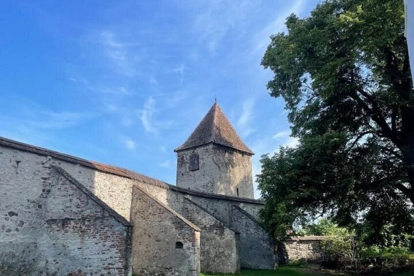 A historic stone building with a tower, surrounded by trees and a clear sky. 3
