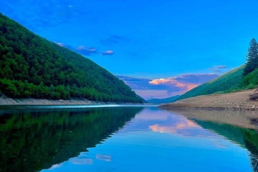 A calm river with a forested hillside on one side and a clear sky above. 1