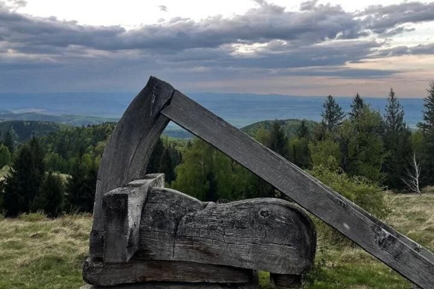 A wooden structure with a curved top, set against a backdrop of a cloudy sky and a distant view of a body of water and forested hills. 2