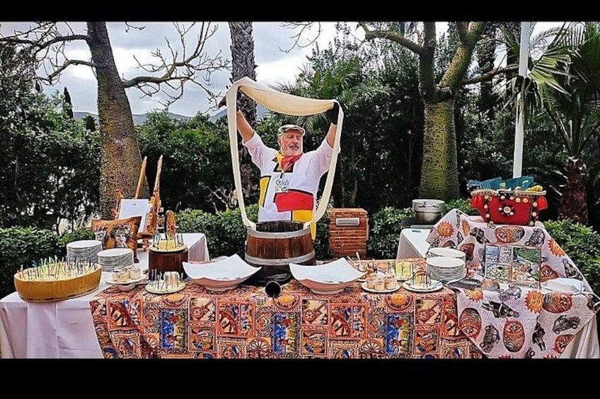 Une personne vêtue d’un costume traditionnel se tient derrière une table où sont disposés des aliments et des boissons. 3