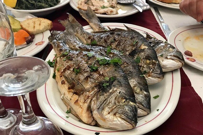 A plate of grilled fish garnished with herbs, accompanied by a glass of white wine and a fork. 5