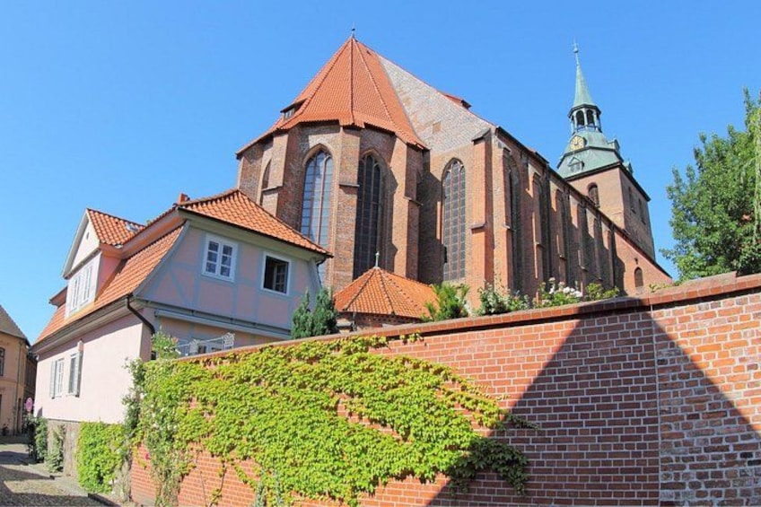A church with a red roof and a green spire, surrounded by a brick wall and a building with a pink facade. 4