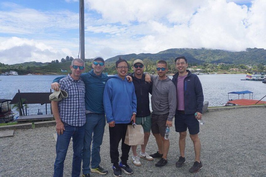 A group of people standing by a lakeside with a boat and a dock in the background. 4