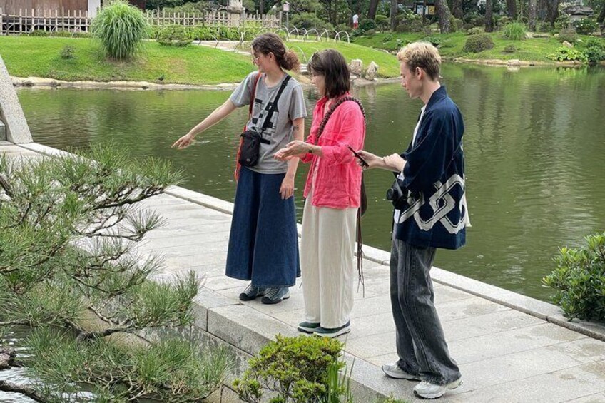 Three people standing by a pond with a bridge in the background. 2