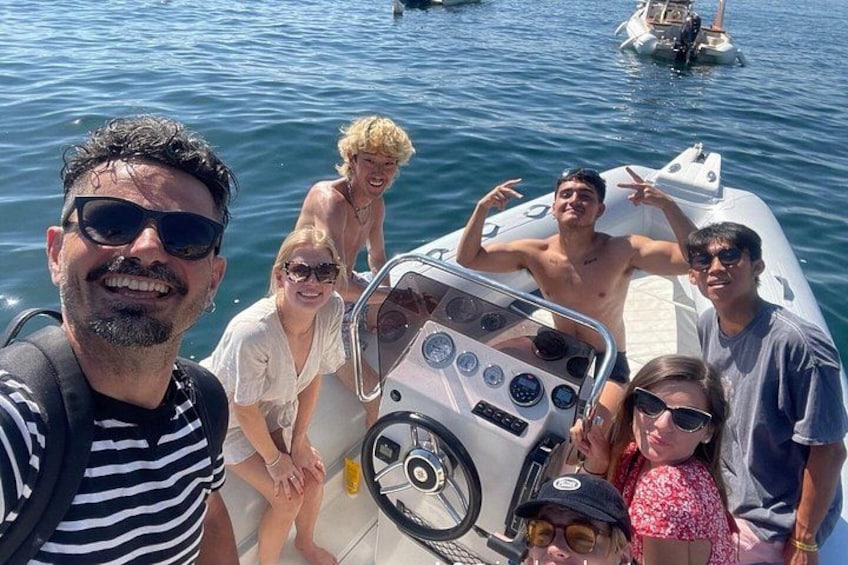 A group of people on a boat with a steering wheel and control panel, surrounded by water and other boats. 2