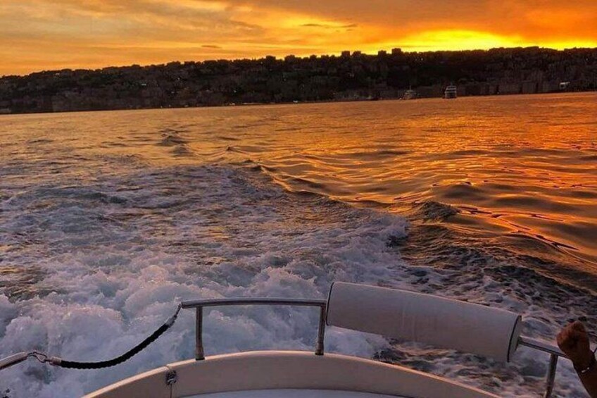 A boat on a body of water with waves, a sunset, and a distant shoreline. 5