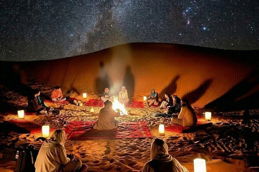 A group of people sitting around a campfire in a desert under a starry sky. 1