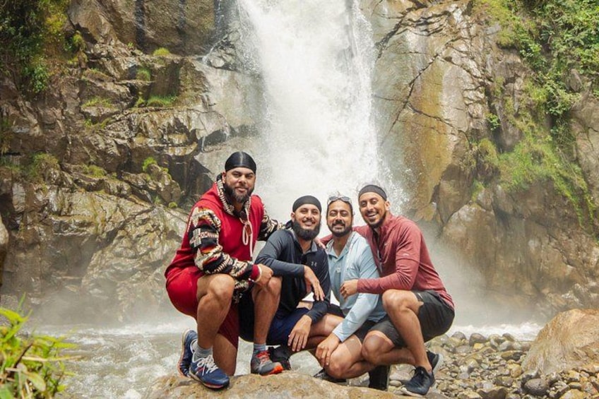 Eine Gruppe von Menschen sitzt auf Felsen in der Nähe eines Wasserfalls in einer felsigen, grünen Landschaft. 4