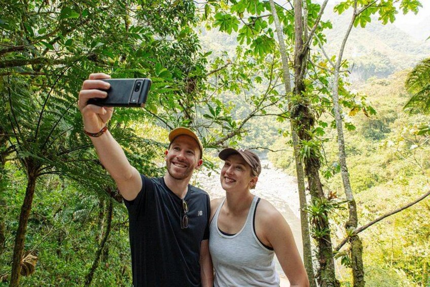 Zwei Personen machen ein Selfie in einem bewaldeten Gebiet, im Hintergrund fließt ein Fluss. 2