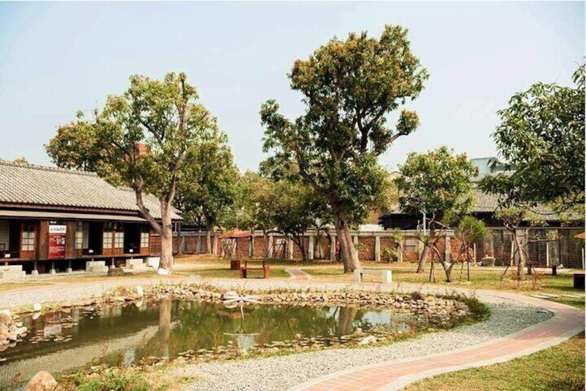 A traditional building with a tiled roof, a small pond, and several trees. 1