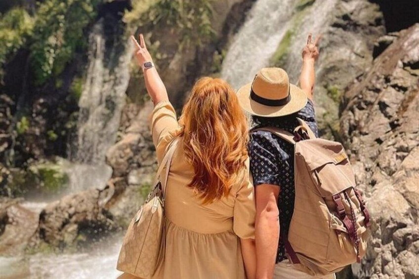 Two people standing by a waterfall, one pointing upwards. 1