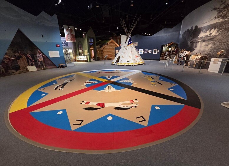 A museum exhibit with a large circular floor design, a teepee, and various artifacts. 2