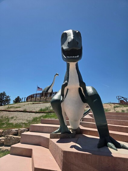 A dinosaur statue on a platform with steps, an American flag, and an ostrich in the background. 3