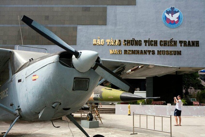 A military helicopter parked in front of a museum with a sign reading 'Bảo Tàng Chúng Tích Chuyên Tranh'. 4