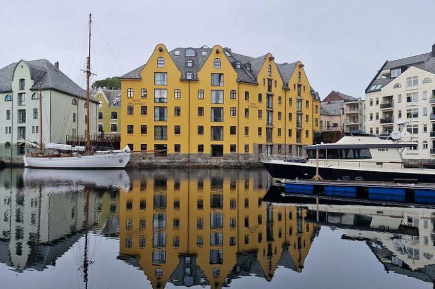 A calm harbor with a yellow building reflecting in the water, a white boat, and a blue boat. 3