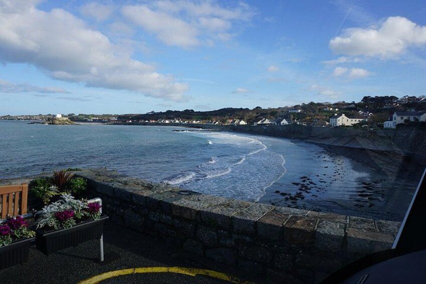 A coastal view with a stone wall, a wooden bench, and a flower bed. 1