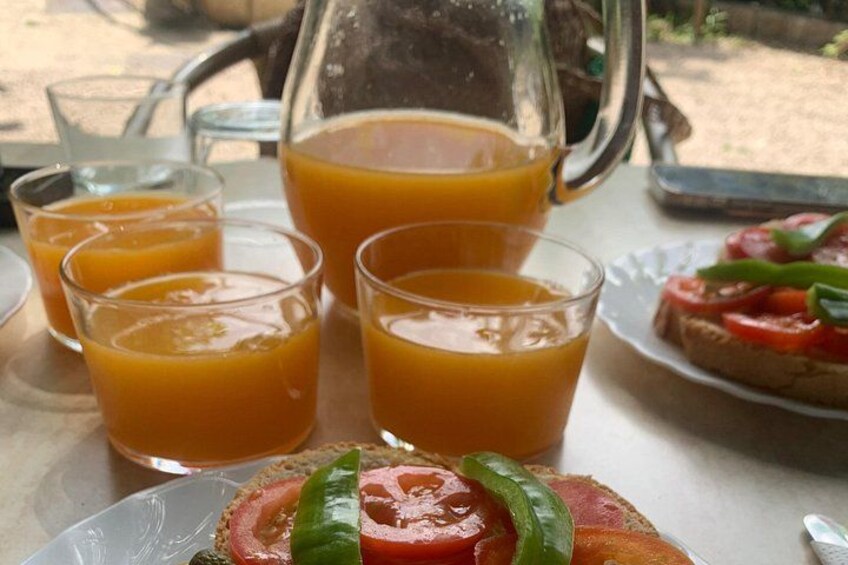 A table with a pitcher of orange juice, four glasses of orange juice, a plate with a sandwich, and a plate with sliced tomatoes and green peppers. 1