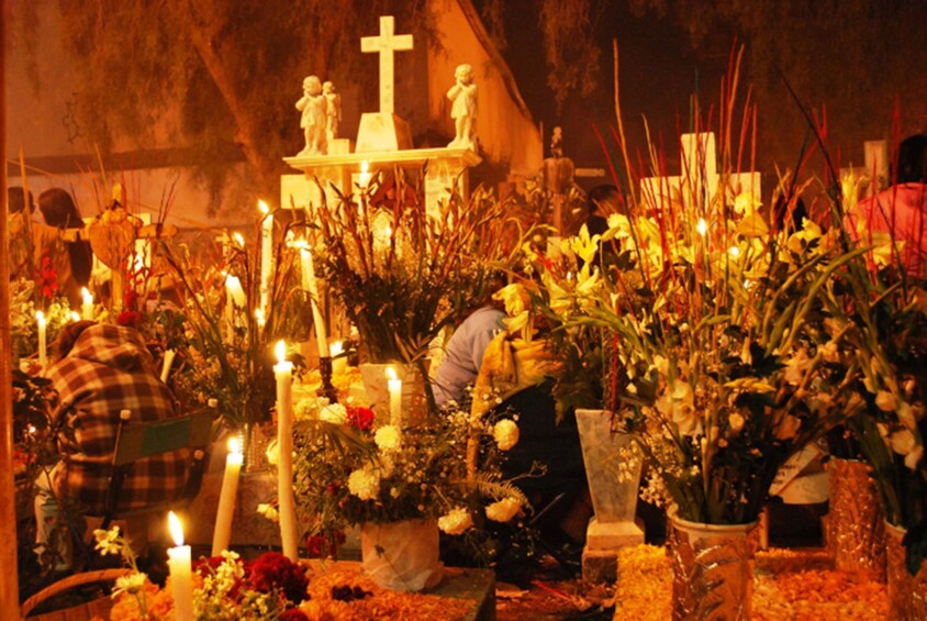 A cemetery with candles, flowers, and a cross. 2