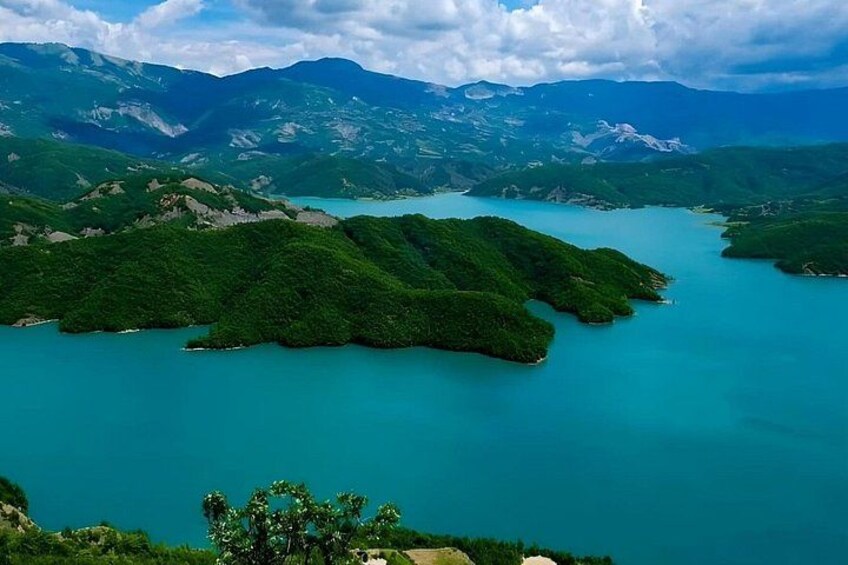 A turquoise lake surrounded by lush green hills and mountains. 1