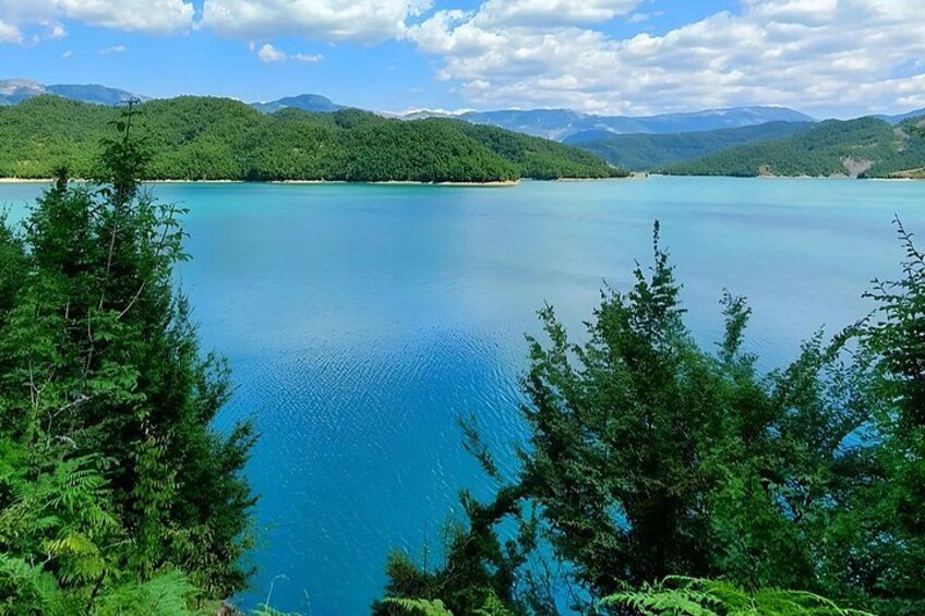 A calm lake surrounded by lush green trees and distant mountains under a partly cloudy sky. 4