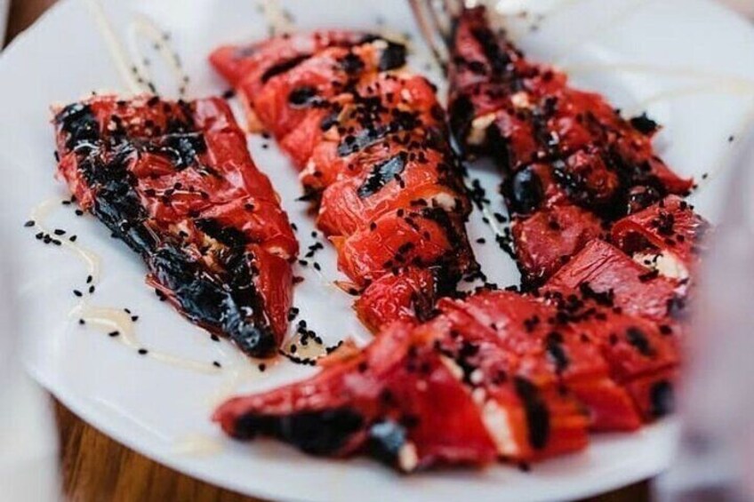 En tallrik med grillade röda paprikor, svarta frön och en skvätt olja. 5