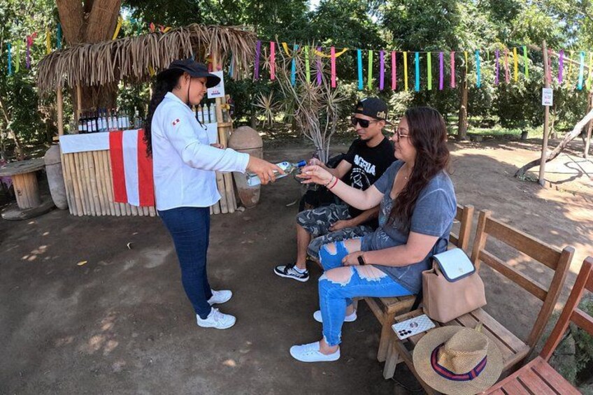 A person handing a card to another seated person, with a thatched structure and colorful flags in the background. 3
