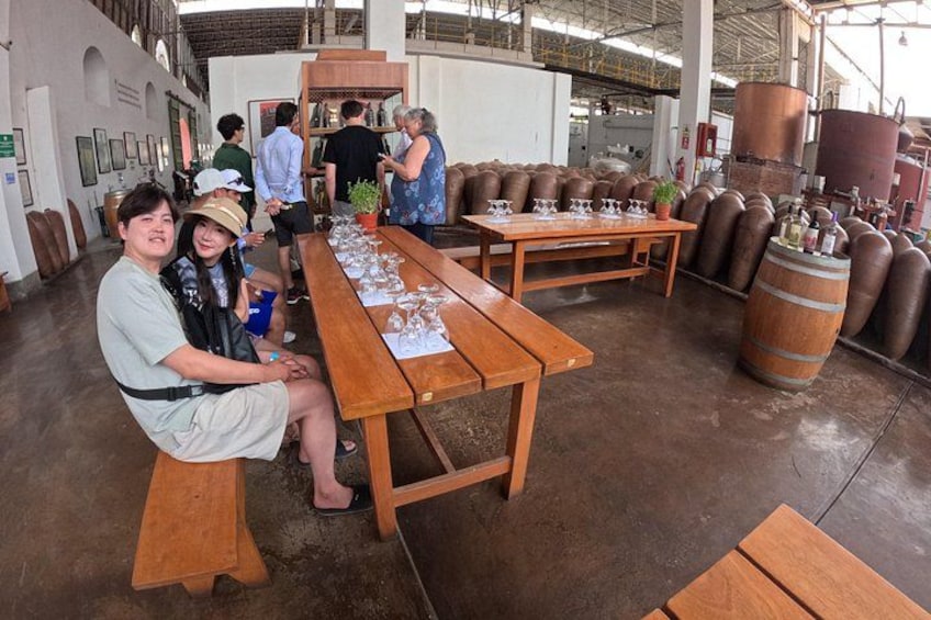 A rustic interior with wooden tables, barrels, and a group of people. 1