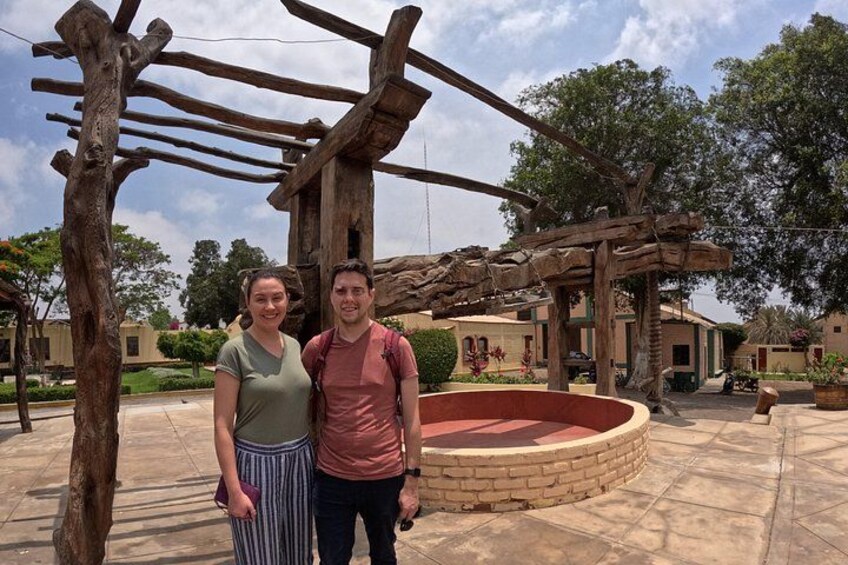 Two people standing in front of a wooden structure with a circular stone feature. 2