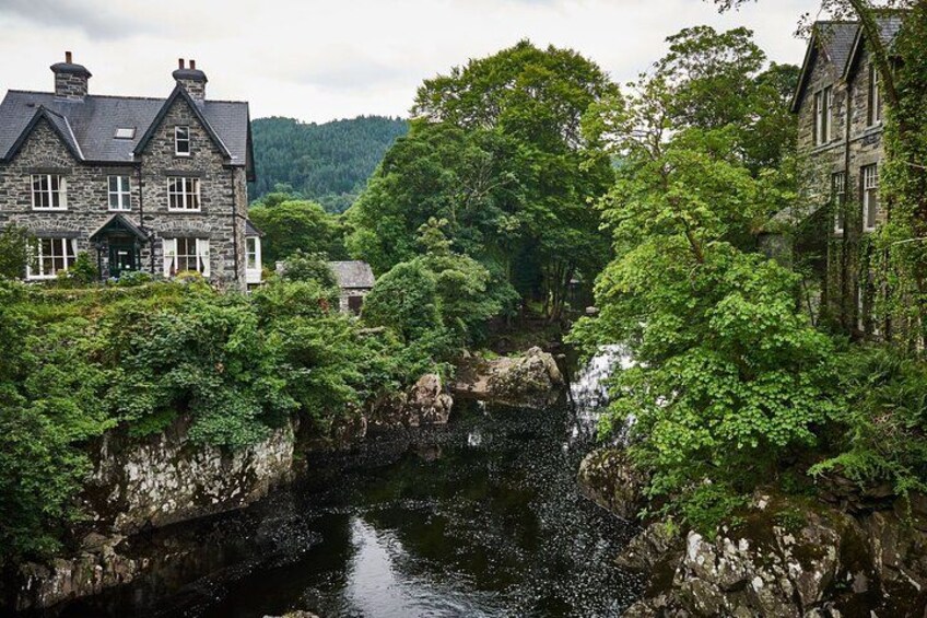 A stone bridge over a river, surrounded by lush greenery and historic stone buildings. 2