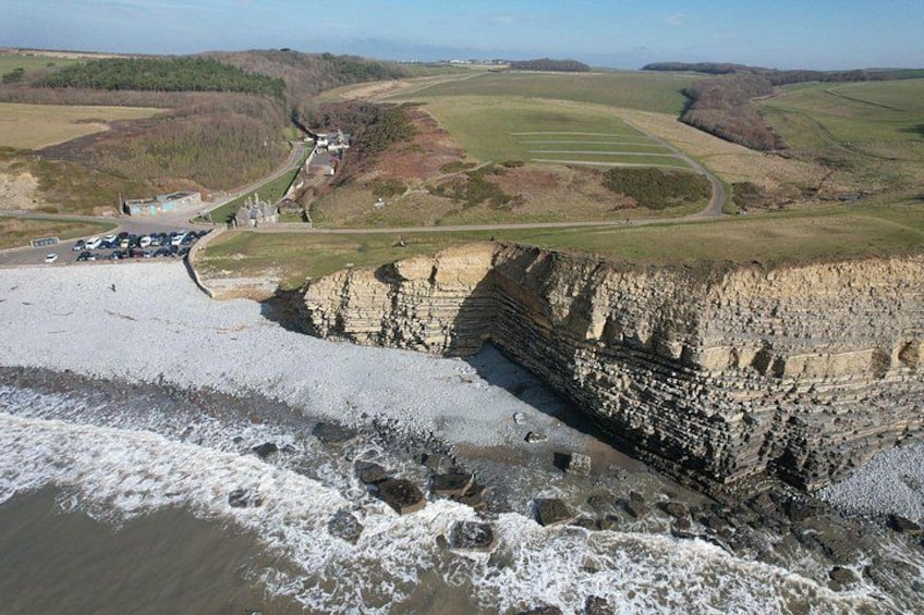 A coastal landscape with cliffs, a beach, and a road leading to a building. 5