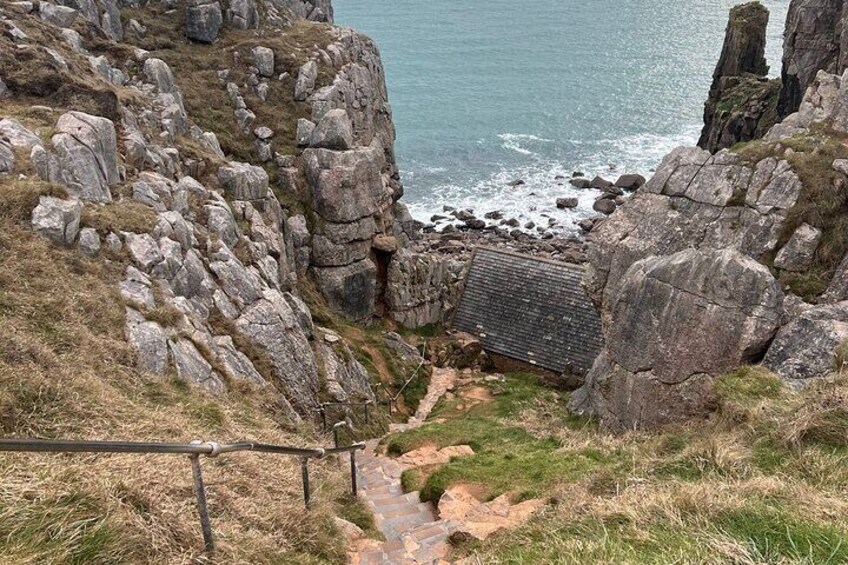 A rocky coastal path with a metal railing, leading to a small shelter near the sea. 5