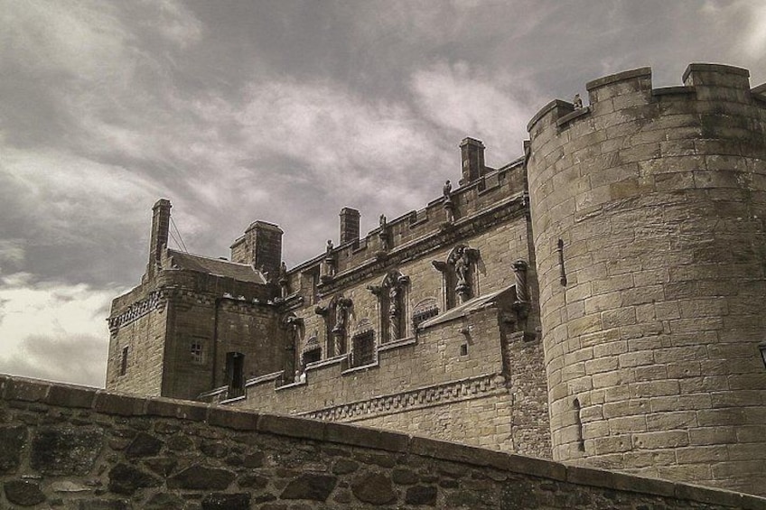 A historic stone castle with battlements, a prominent tower, and a large arched window. 4