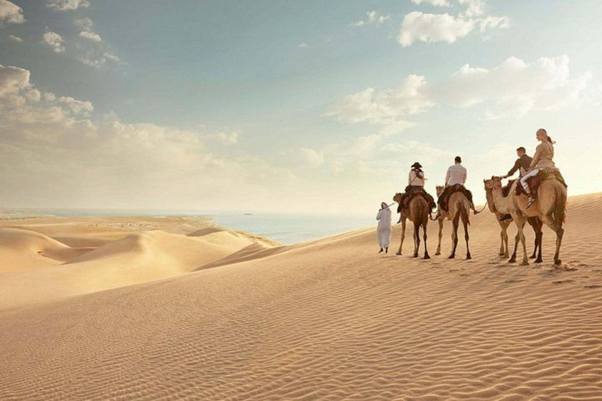A desert landscape with sand dunes and a group of people riding camels. 2