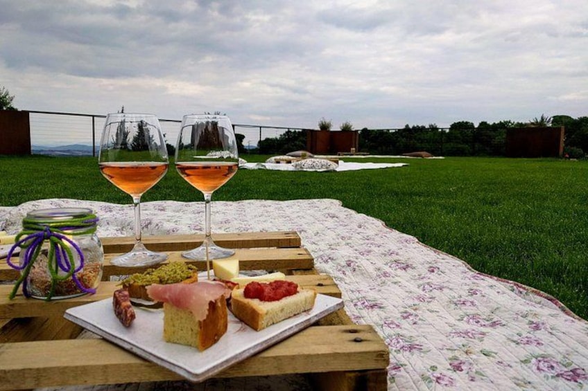 Un montaje para picnic con manta, comida y copas de vino sobre una mesa de madera en un área cubierta de césped. 4