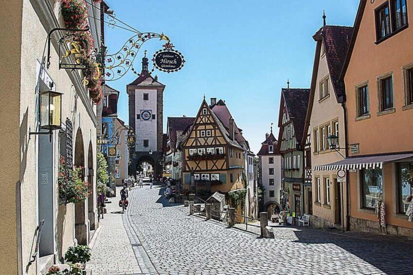 A cobblestone street lined with traditional half-timbered houses, a clock tower, and a sign for a restaurant. 3