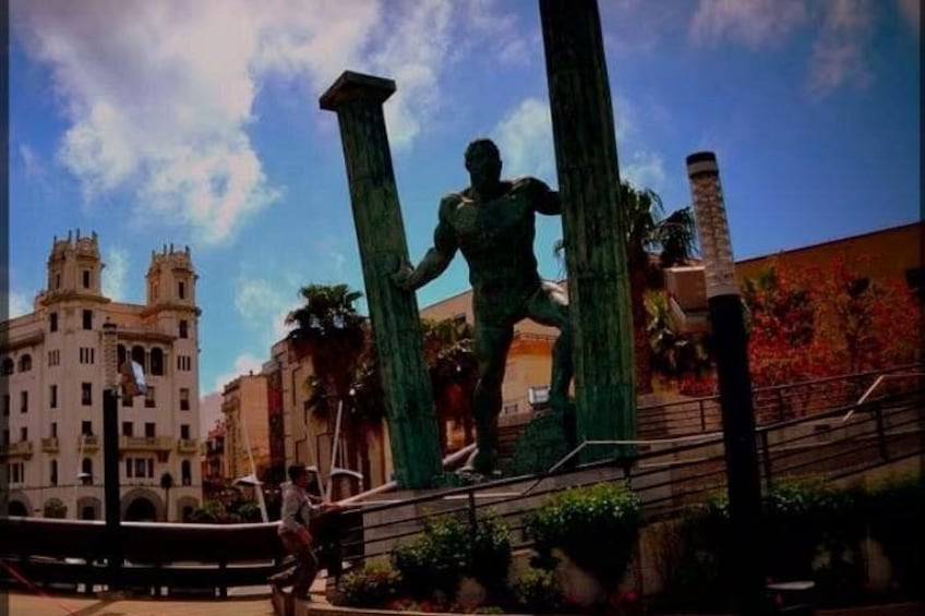 A statue of a man climbing a column, a historic building in the background, and a clear sky. 1