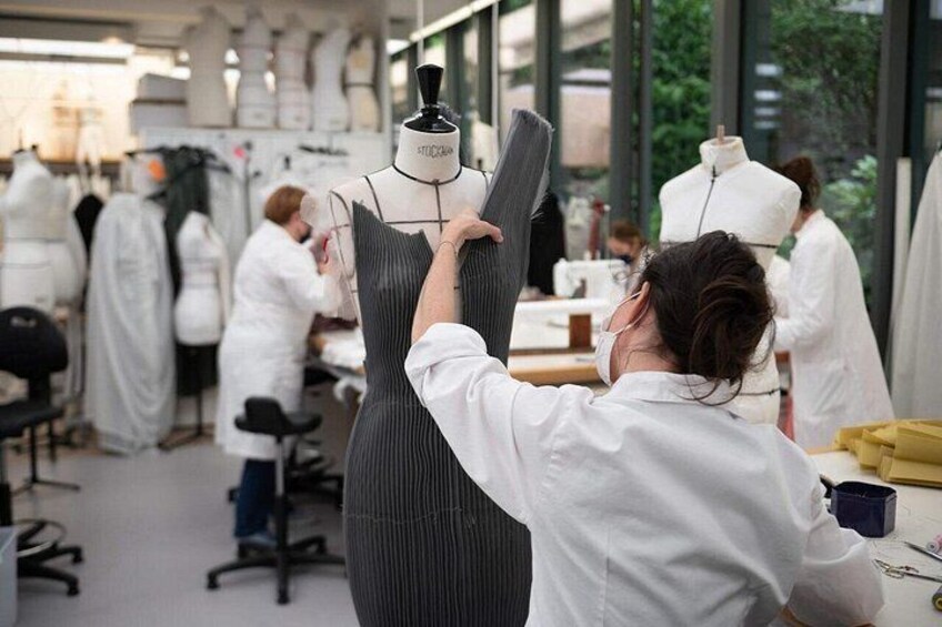 A person adjusting a mannequin in a workshop with sewing machines and fabric in the background. 2