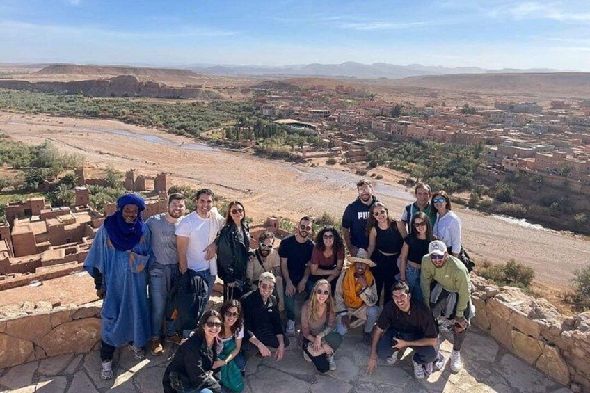 A group of people posing on a stone platform overlooking a valley with traditional buildings and a river. 3