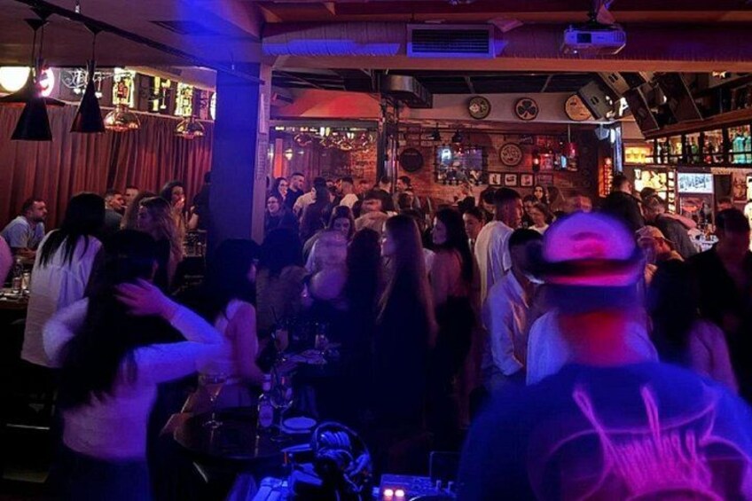 A crowded bar with people socializing and music playing in the background. 4