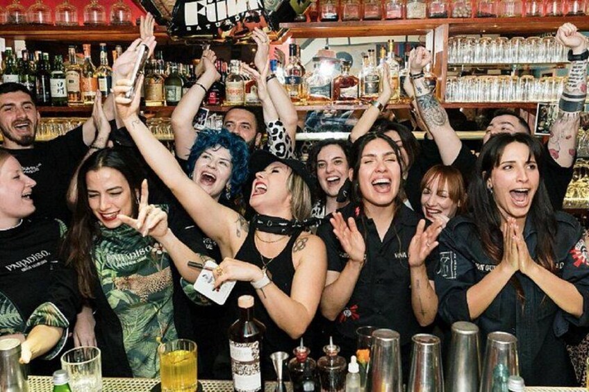 Un gruppo di persone al bar, con bottiglie e bicchieri sul bancone. 1